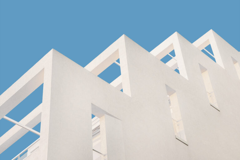 Erstrangige Finanzierung. Moderne geometrische Architektur mit weißem Beton und minimalistischer Fassade in klarem Himmel.