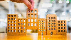 Hand selecting miniature wooden house models for real estate investment on a wooden table.